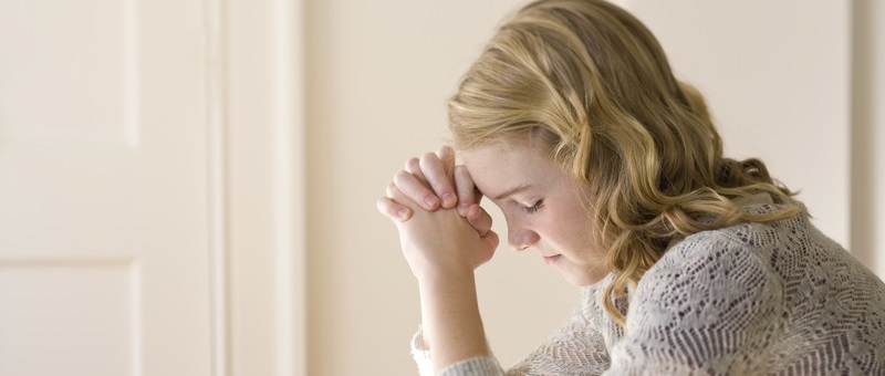 Photo of a young woman kneeling by her bed and praying